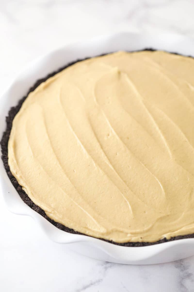 Spreading peanut butter pie filling into an Oreo crust in a pie pan.