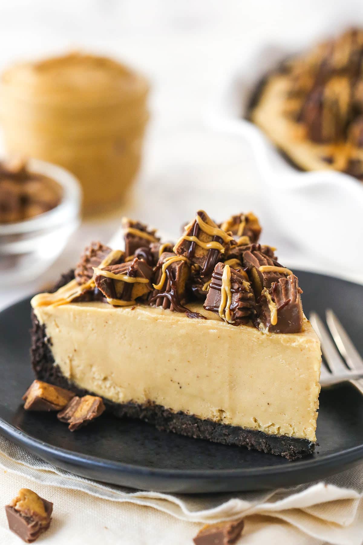 Reese's peanut butter pie is made of Oreo crust with peanut butter filling topped with Reese's, chocolate ganache, and peanut butter. A slice of Reese's peanut butter pie on a plate with a fork.