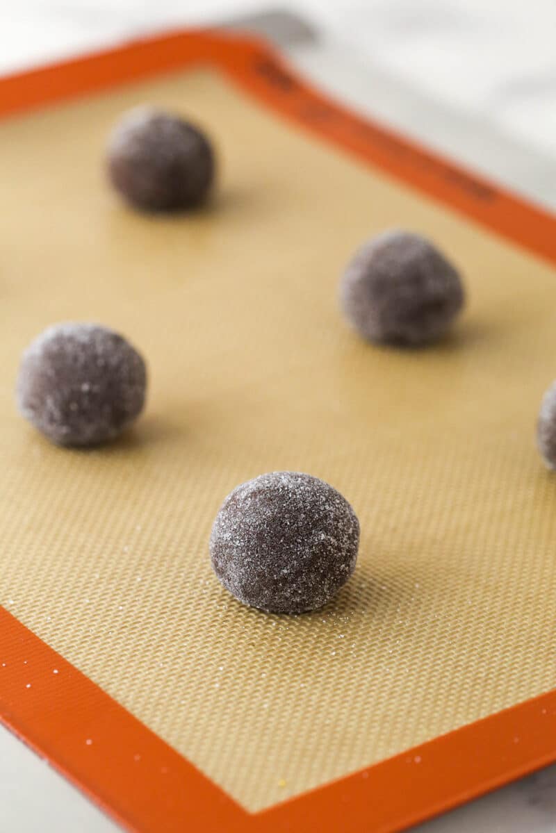 Chocolate sugar cookie dough formed into balls and arranged on a silicone baking mat.