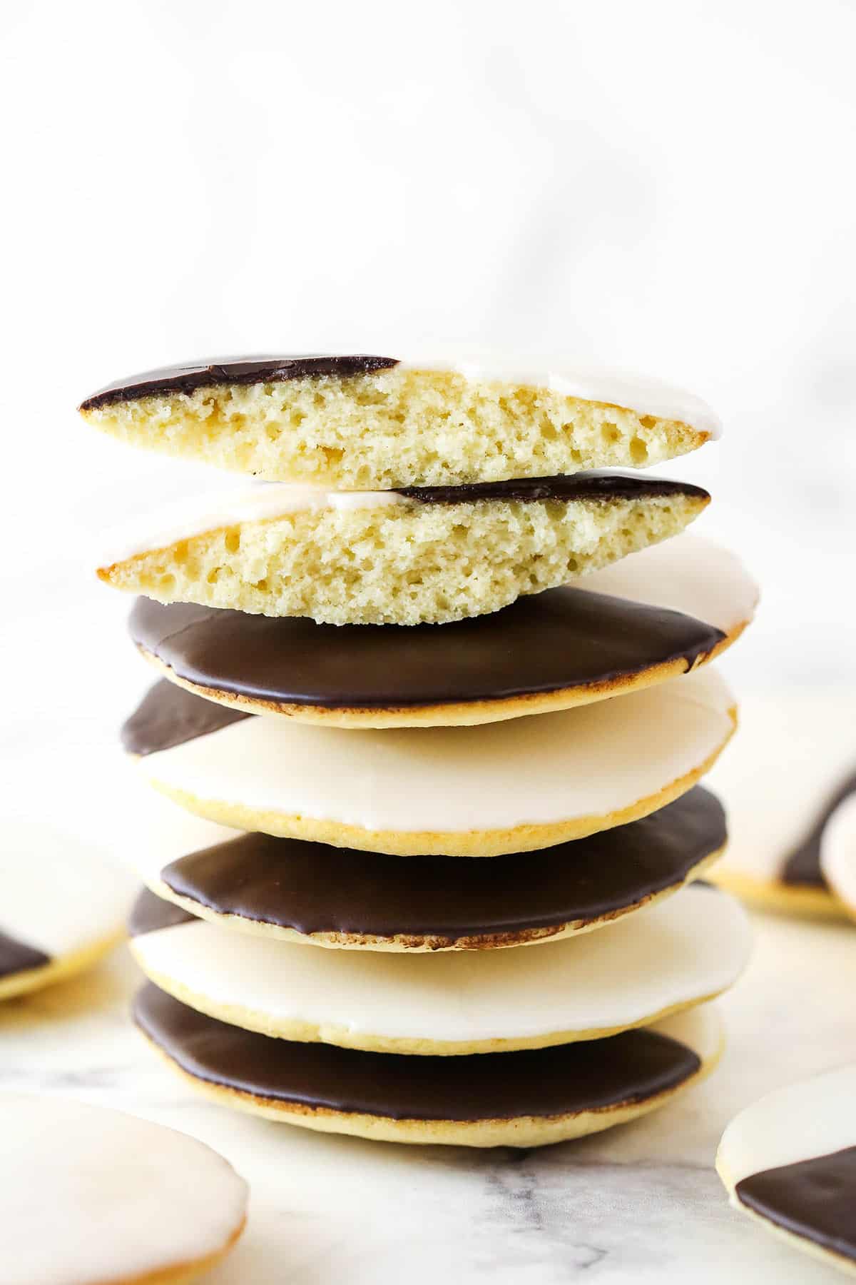 Black and white cookies are soft, cakey vanilla cookies topped with both "black" (chocolate) and white icing. Tres elegant! A stack of black and white cookies. The top cookie is broken in half.