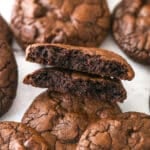 Brownie cookies scattered on a marble surface. One is broken in half.