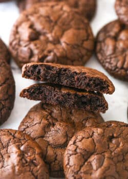 Brownie cookies scattered on a marble surface. One is broken in half.