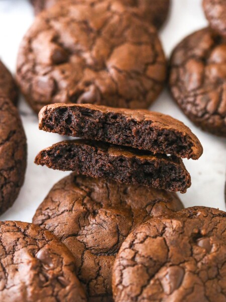 Brownie cookies scattered on a marble surface. One is broken in half.