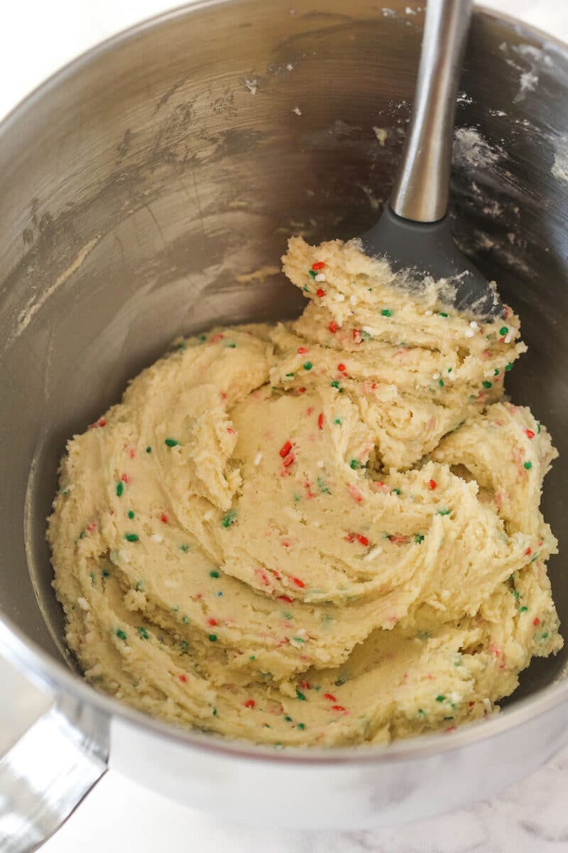Frosting in a silver mixing bowl that has Christmas sprinkles in it.