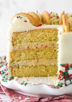 Frosted Sugar Cookie Layer Cake on a white cake plate with several slices removed to show layers.