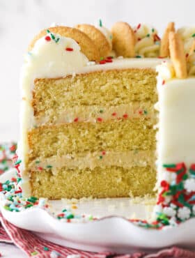 Frosted Sugar Cookie Layer Cake on a white cake plate with several slices removed to show layers.