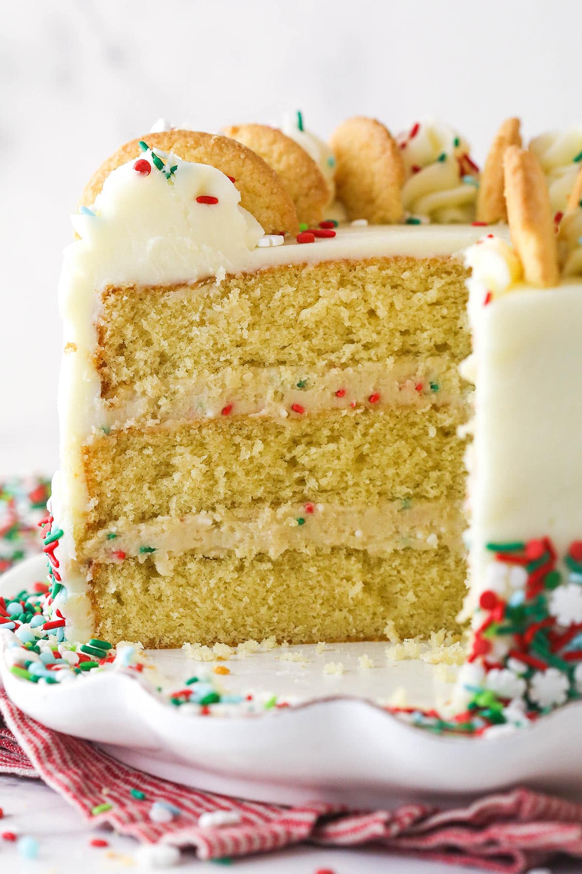 Frosted Sugar Cookie Layer Cake on a white cake plate with several slices removed to show layers.