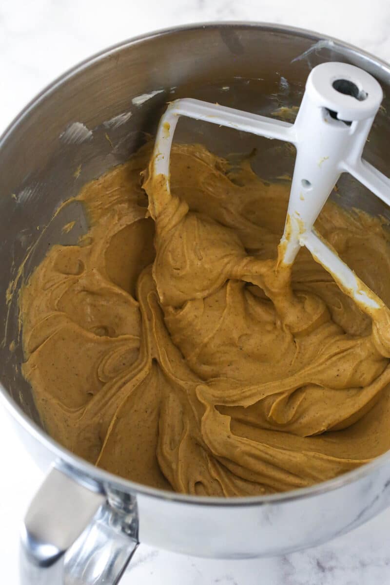 Cream cheese and sugar mixture with added spices in a metal mixing bowl.