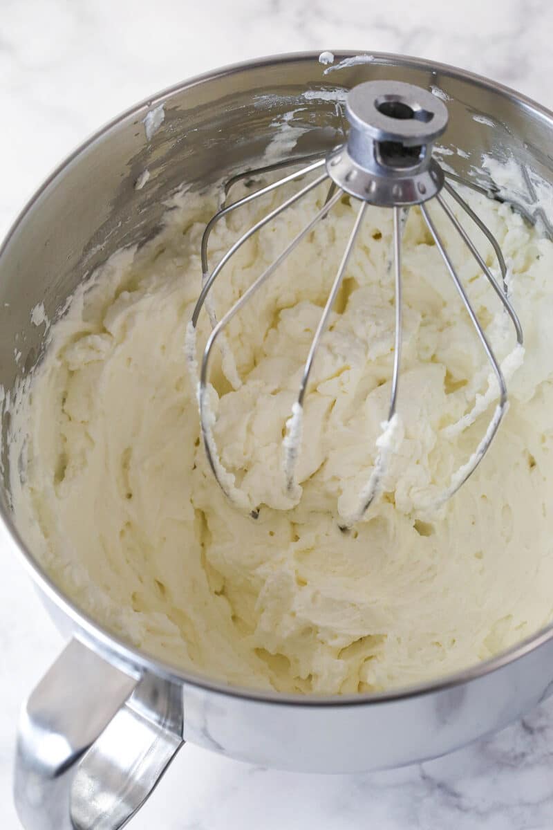 Whipped cream with stiff peaks in a metal mixing bowl.