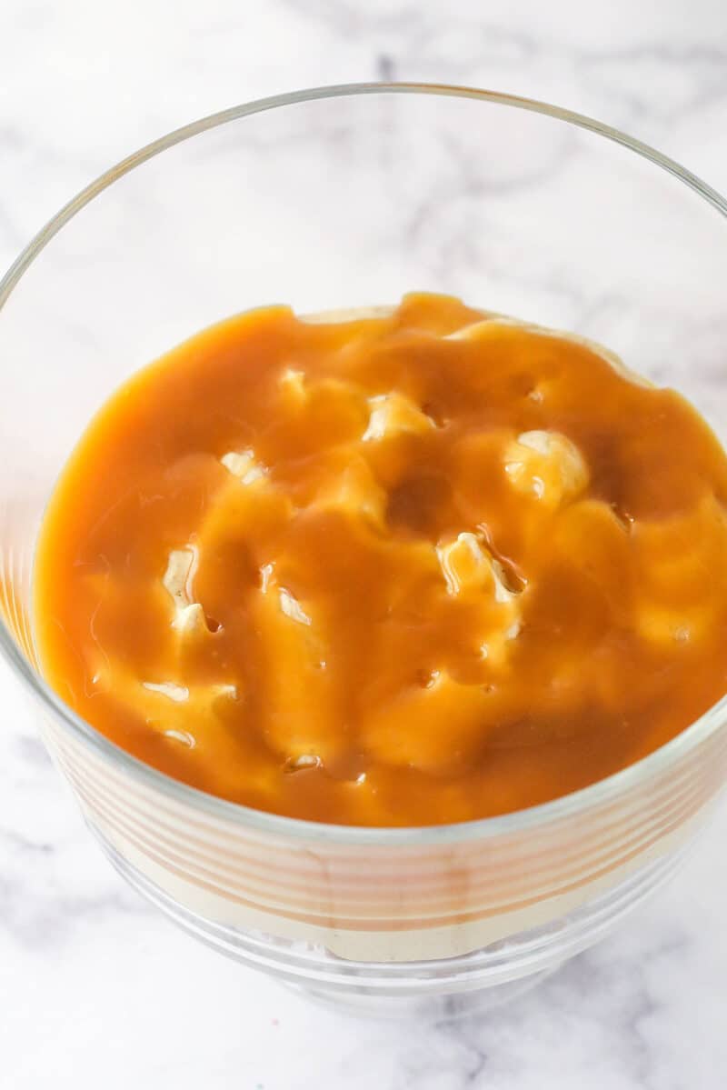 A glass trifle bowl with a layer of caramel sauce.