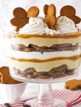 Close up of a Gingerbread Cheesecake Trifle in a trifle bowl on a striped napkin.