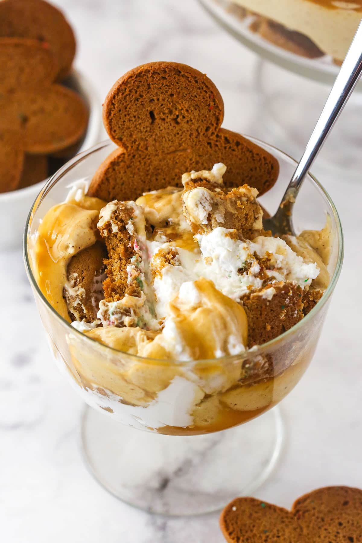 Gingerbread Cheesecake Trifle in a small glass serving bowl with a spoon inserted.