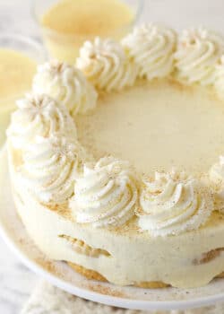 A No Bake Eggnog Icebox Cake on a white cake plate with eggnog in the background.