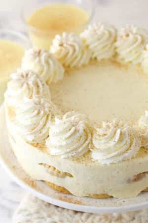 A No Bake Eggnog Icebox Cake on a white cake plate with eggnog in the background.