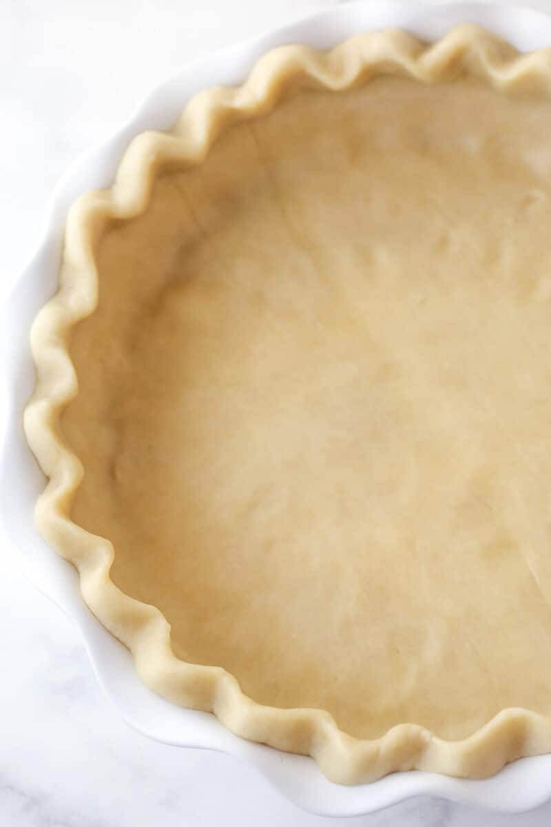 This pecan pie recipe features a luscious, buttery filling loaded with pecans & bursting with the rich flavors of dark brown sugar & vanilla. Crust pressed into a white pie pan.