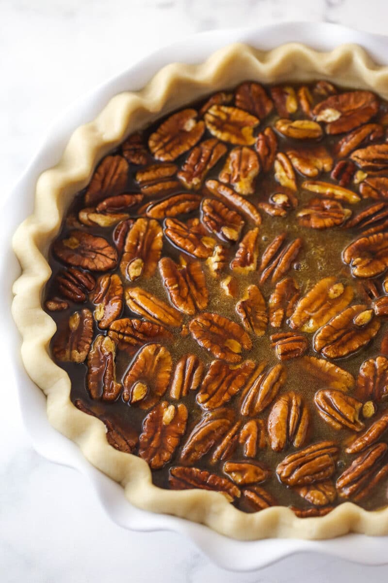 A white pie plate filled with pecan pie filling and pecans