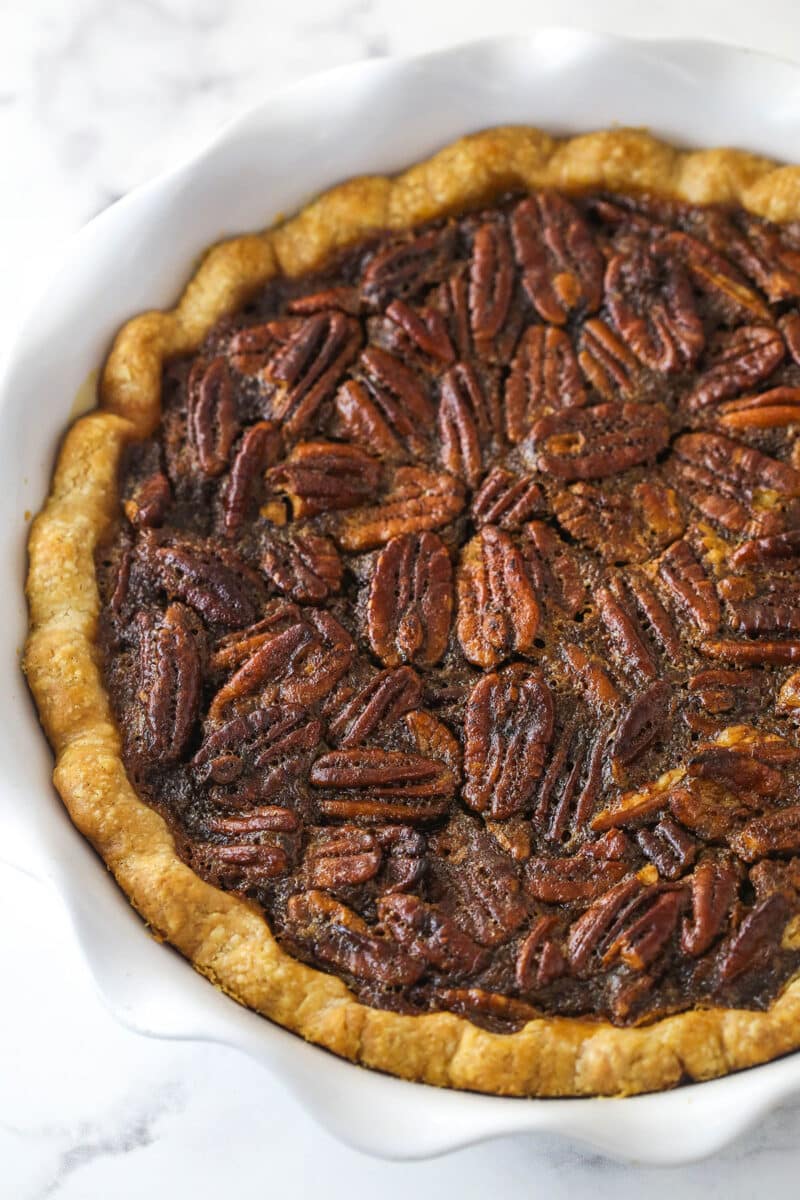 This pecan pie recipe features a luscious, buttery filling loaded with pecans & bursting with the rich flavors of dark brown sugar & vanilla. A baked Classic Pecan Pie in a white pie plate.