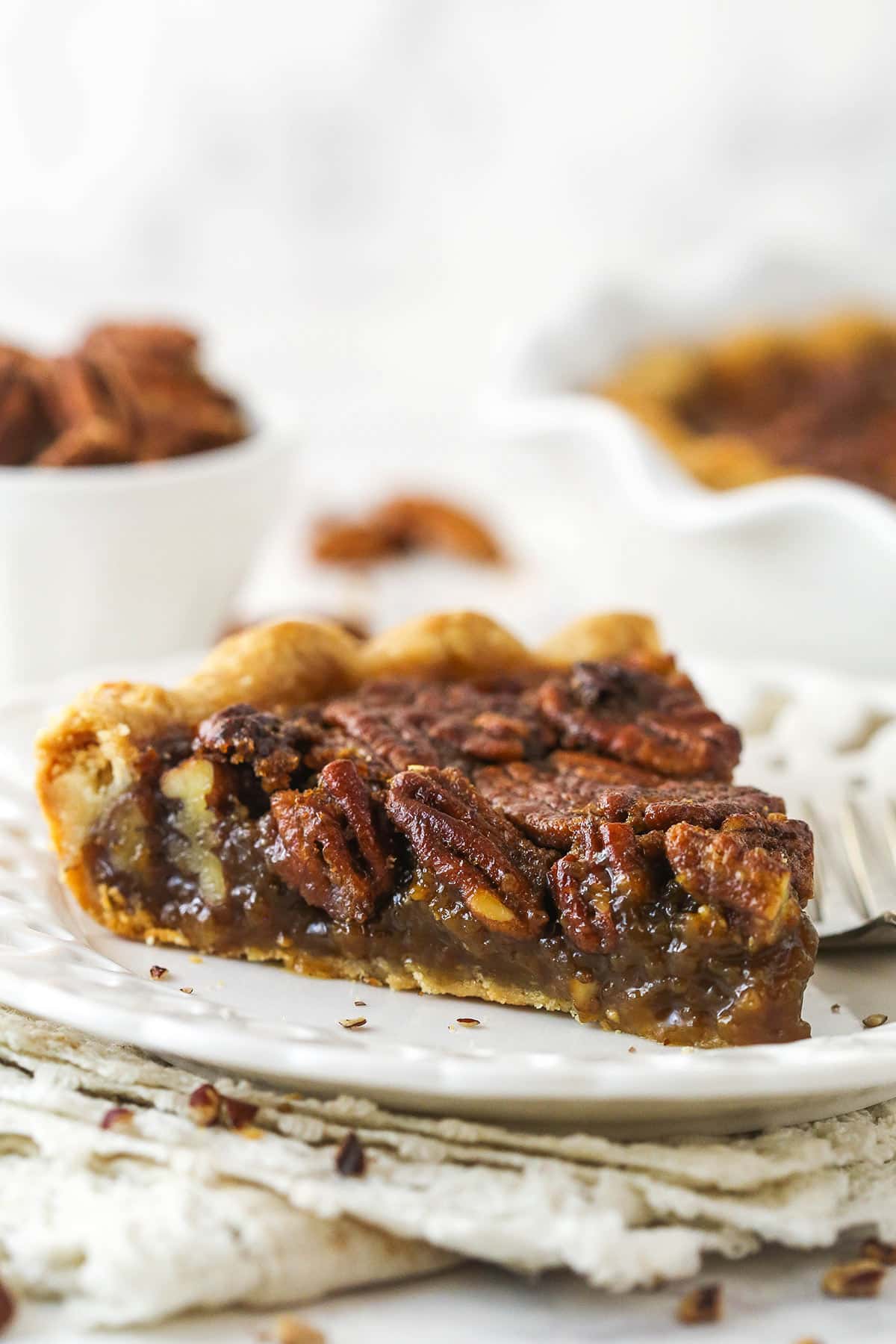 This pecan pie recipe features a luscious, buttery filling loaded with pecans & bursting with the rich flavors of dark brown sugar & vanilla. A slice of Classic Pecan Pie on a white plate.