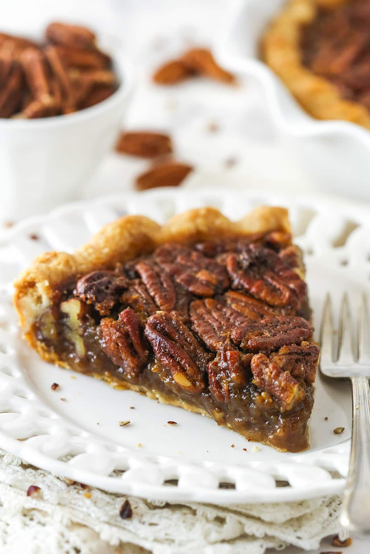 A slice of Classic Pecan Pie in a white plate next to a fork.