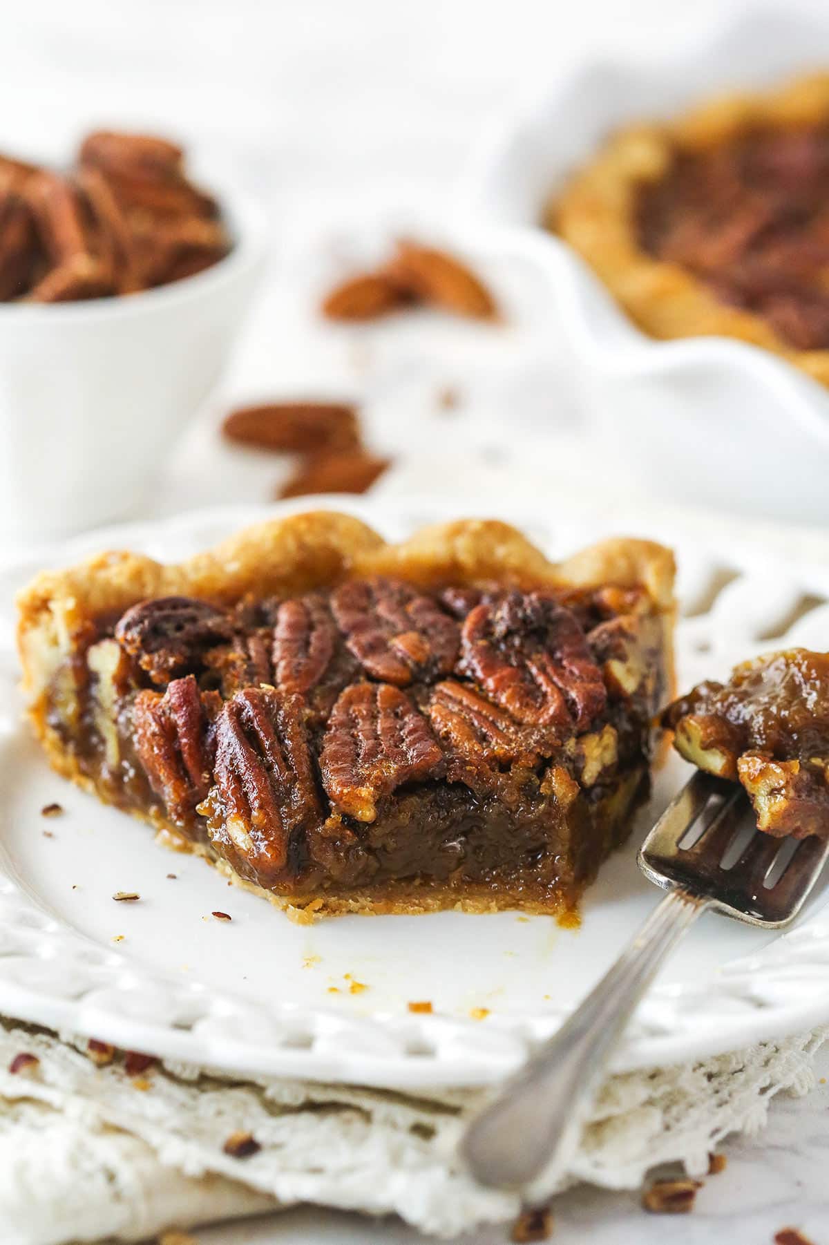 A slice of Classic Pecan Pie on a white plate with a bite removed with a fork.