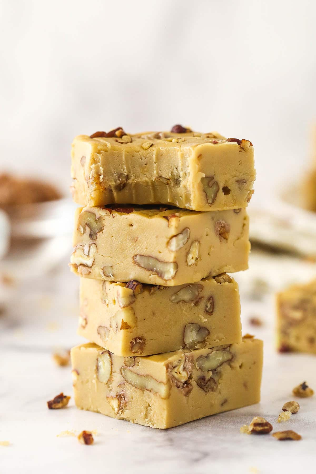 Pecan Pralines Fudge is rich and buttery, chock full of toasted pecans, and has unbelievable melt-in-you-mouth brown sugar flavor! Plus, it's simple to make! 4 pieces of Praline Pecan Fudge stacked one on top of the other with a bite removed from the top piece.