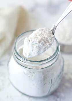 A spoon scooping heat treated flour out of a jar.