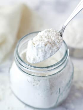 A spoon scooping heat treated flour out of a jar.