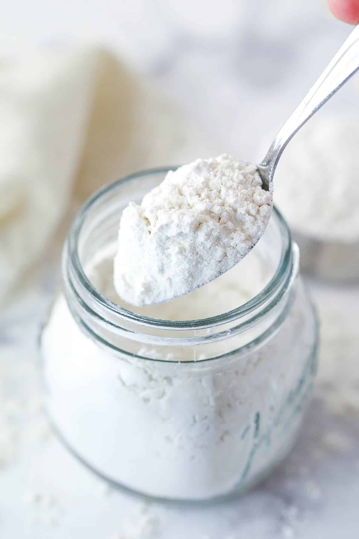 A spoon scooping heat treated flour out of a jar.