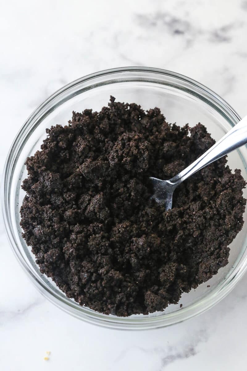 Mixing together Oreo cookie crumbs and butter to make Oreo crust.