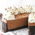 A No-Bake Chocolate Cheesecake on a white serving plate with a slice removed to show texture.