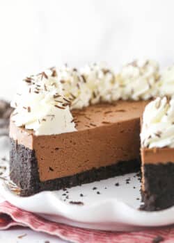 A No-Bake Chocolate Cheesecake on a white serving plate with a slice removed to show texture.