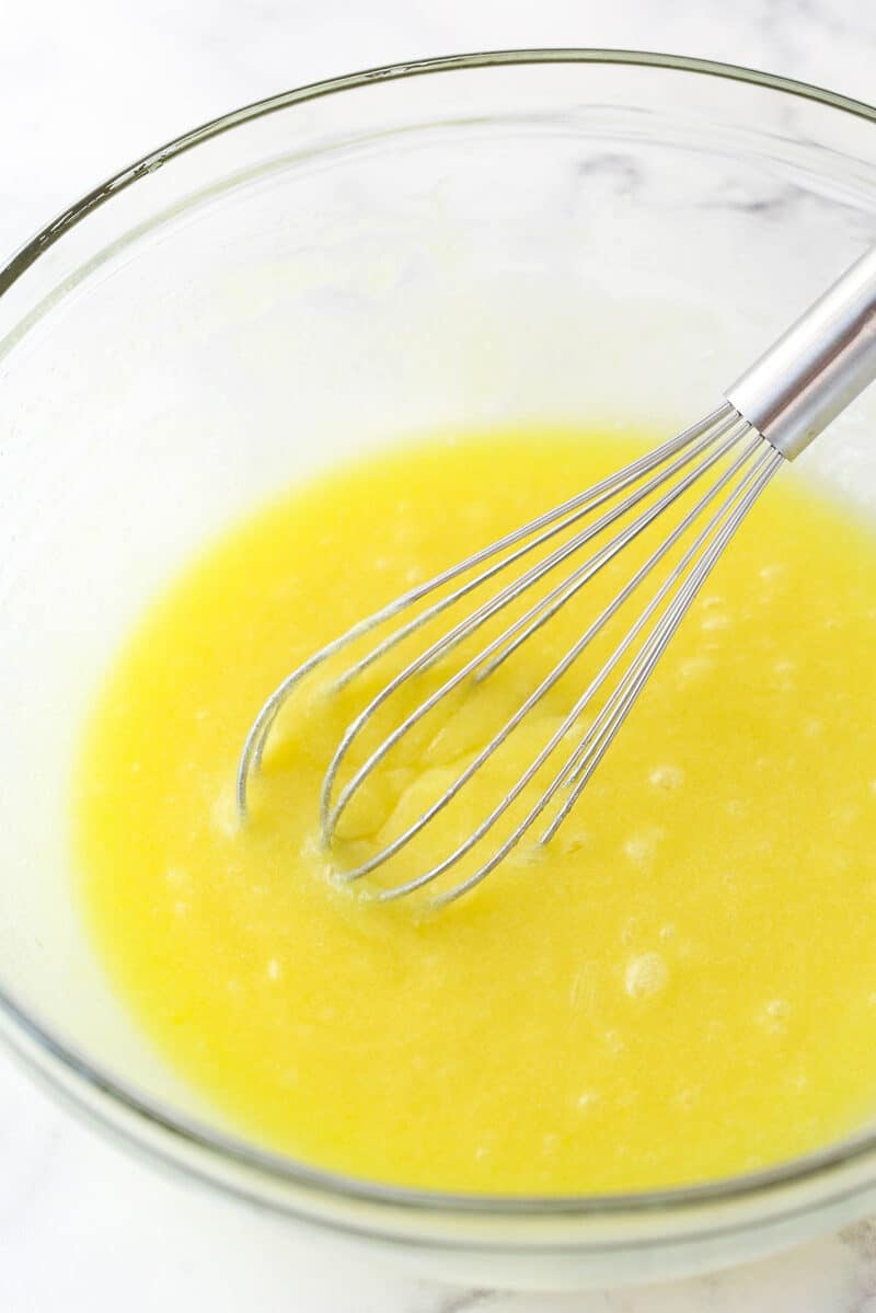 Whisking eggs into melted butter, sugar, and vanilla.