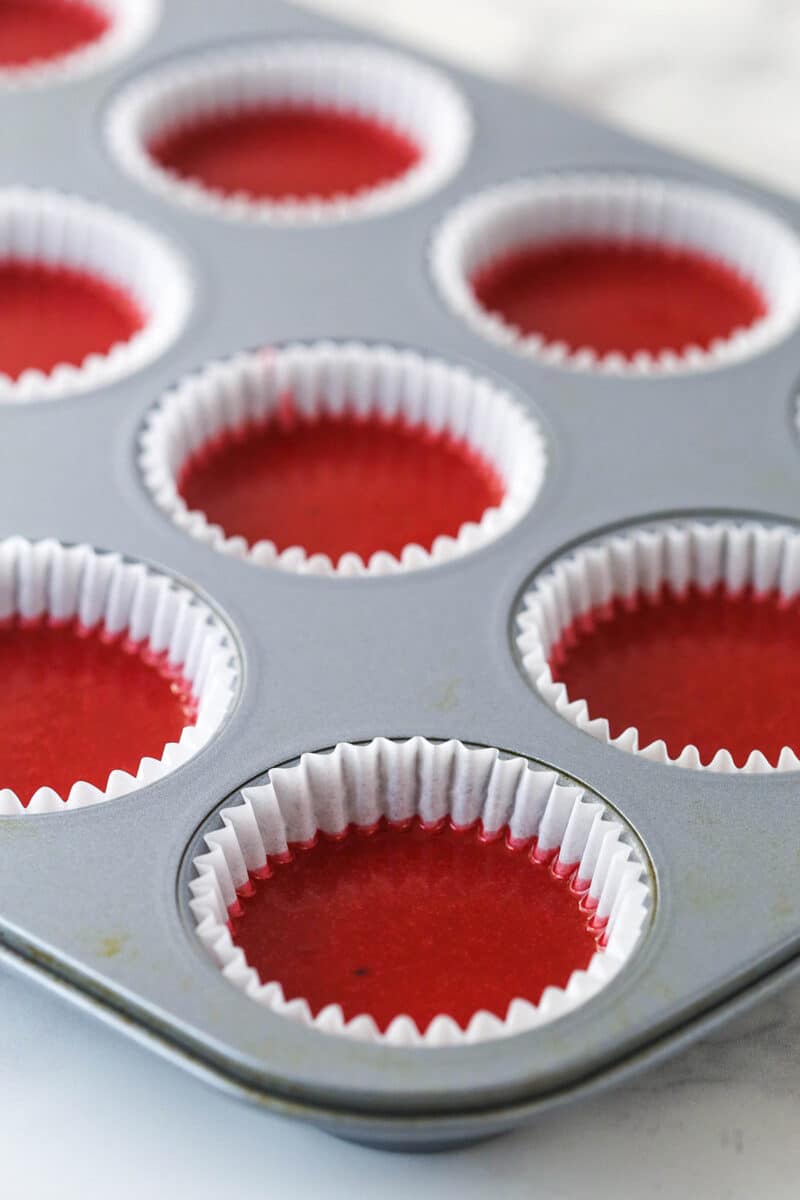 Red velvet cupcake batter in cupcakes liners in a cupcake pan.