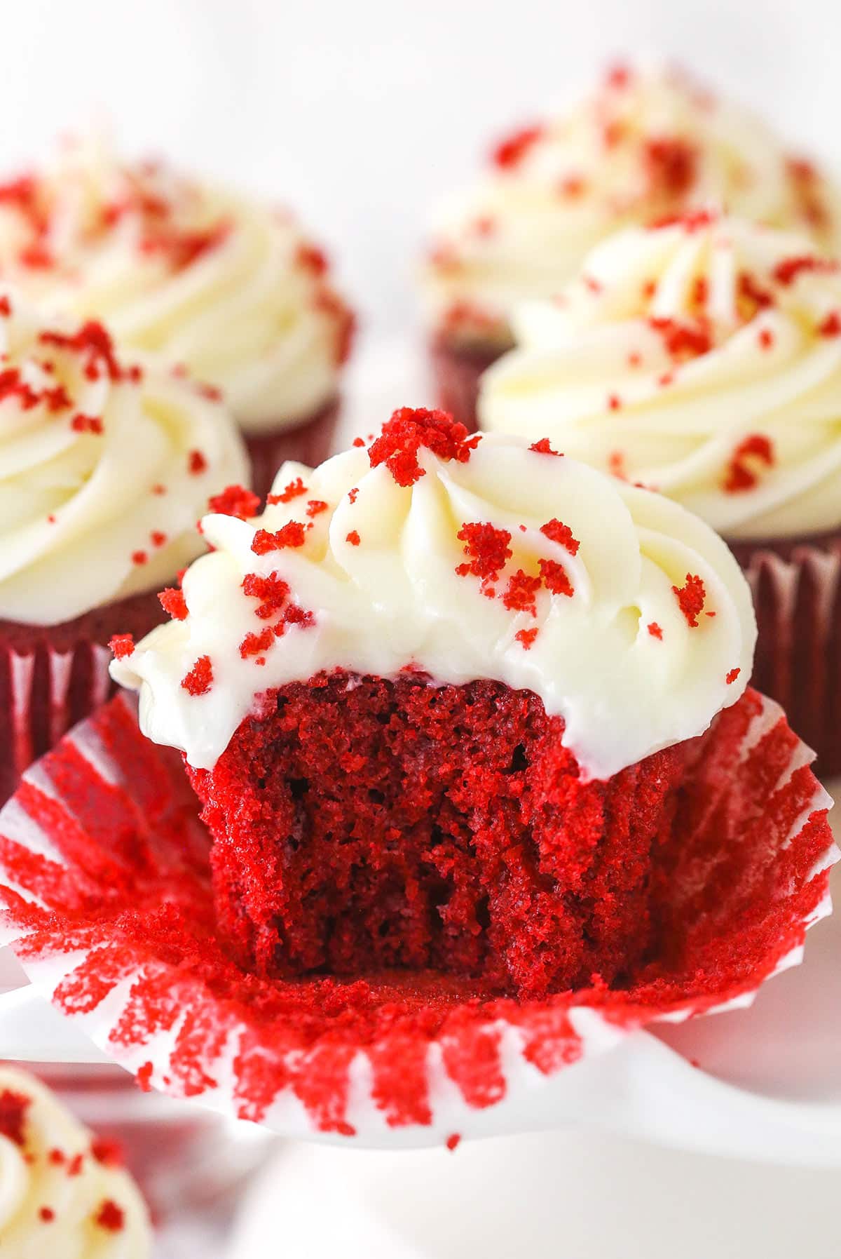 Red velvet cupcakes on a serving platter. One has a bite taken out of it.