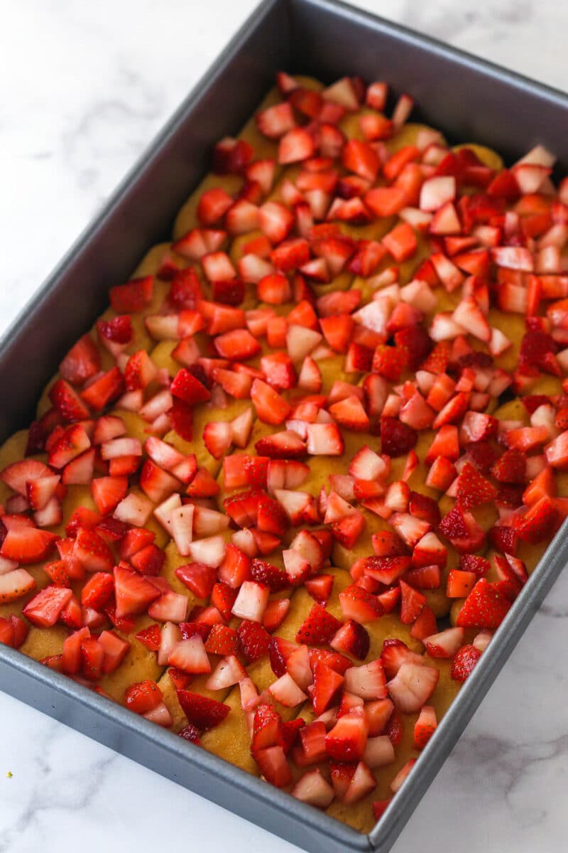 Layers of lady fingers and chopped strawberries in a metal baking pan for Strawberry Champagne Tiramisu.