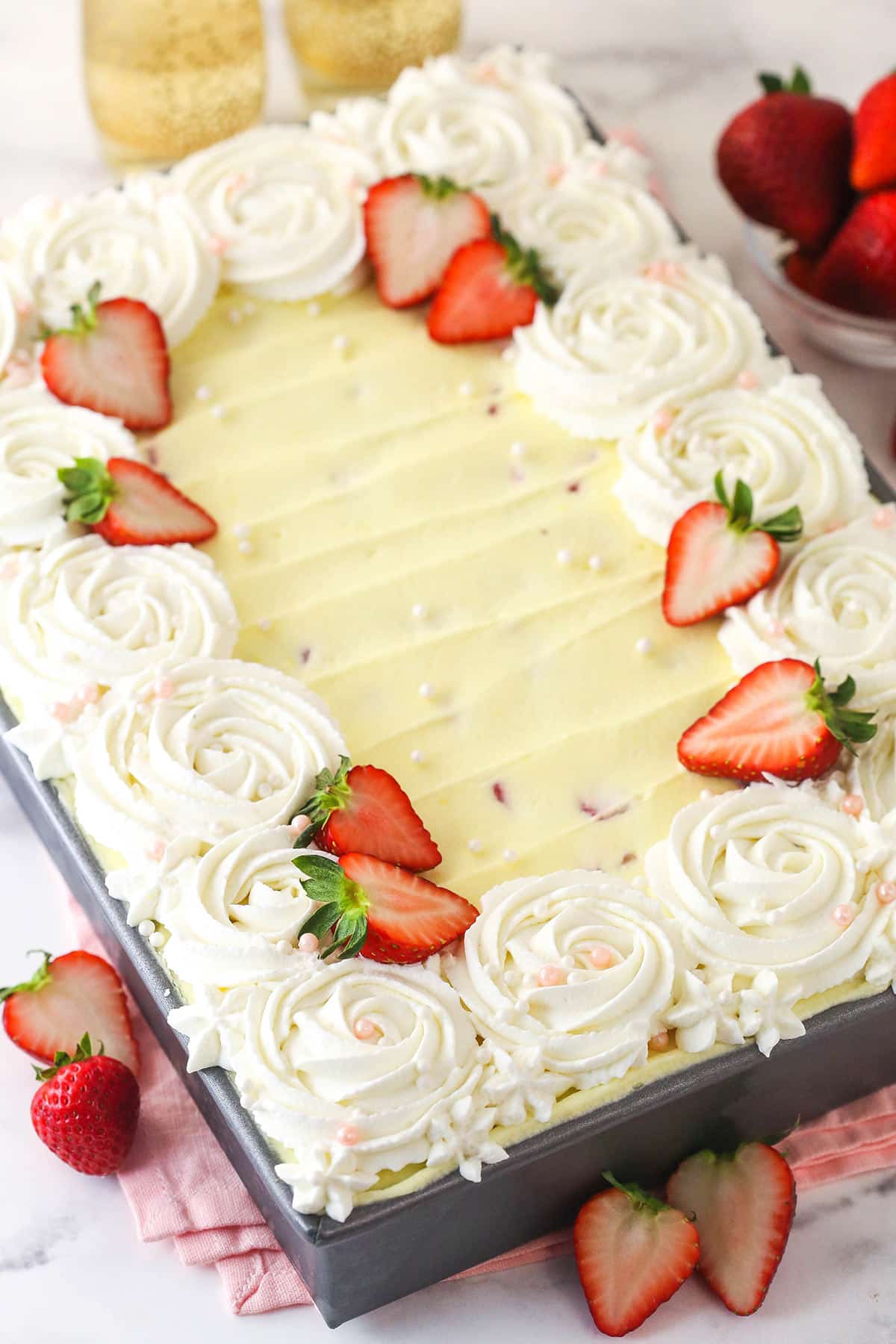 Strawberry Champagne Tiramisu is such a fun and tasty twist on classic tiramisu. Ladyfingers are dipped in a lightly-sweet champagne mixture and layered with chopped strawberries and delicious mascarpone filling. Strawberry Champagne Tiramisu decorated with strawberries in a metal pan.