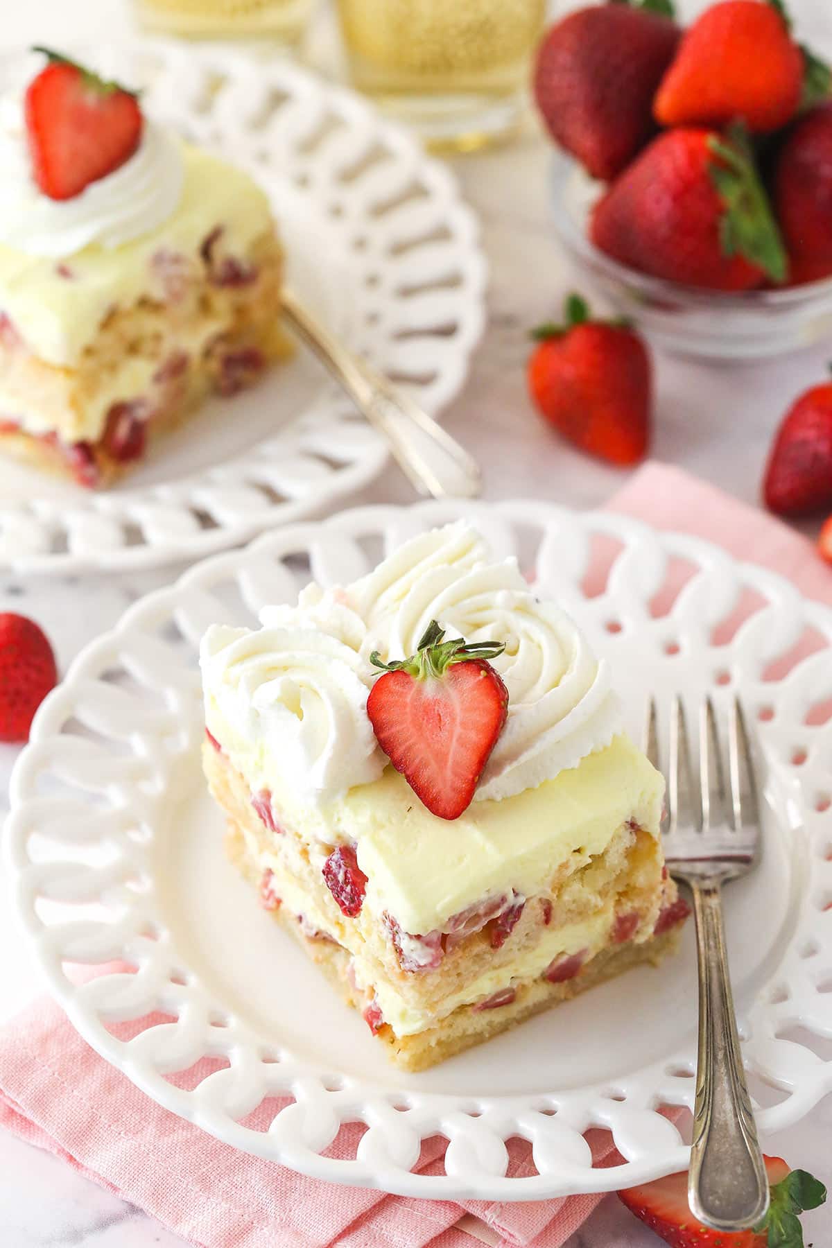 Strawberry Champagne Tiramisu is such a fun and tasty twist on classic tiramisu. Ladyfingers are dipped in a lightly-sweet champagne mixture and layered with chopped strawberries and delicious mascarpone filling. Top view of a slice of Strawberry Champagne Tiramisu on a white plate and pink napkin.