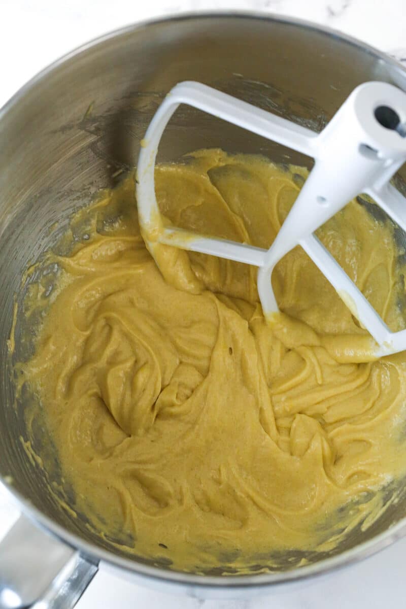 Mixing eggs into creamed butter, oil, eggs, sugars, and vanilla.