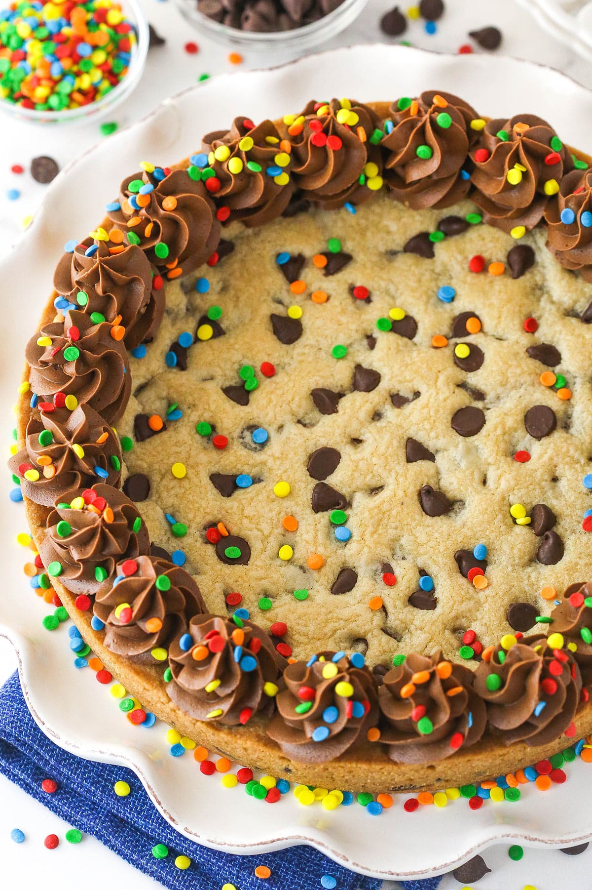 Chocolate chip cookie cake is so moist and chewy and is absolutely loaded with chocolate chips. It's even topped with chocolate buttercream! Chocolate Chip Cookie Cake with multicolored sprinkles on a serving platter.