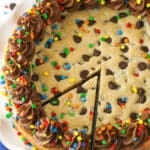 A full Chocolate Chip Cookie Cake with a slice cut out on a white platter.