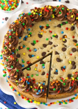 A full Chocolate Chip Cookie Cake with a slice cut out on a white platter.