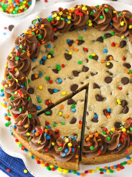 A full Chocolate Chip Cookie Cake with a slice cut out on a white platter.
