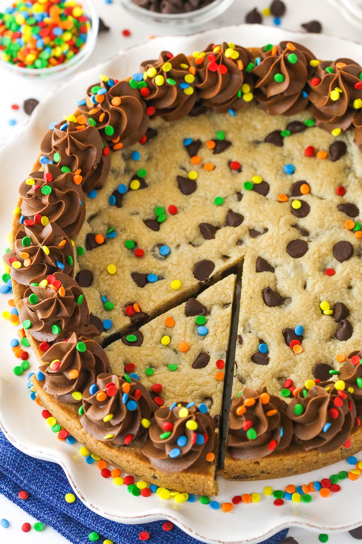 A full Chocolate Chip Cookie Cake with a slice cut out on a white platter.