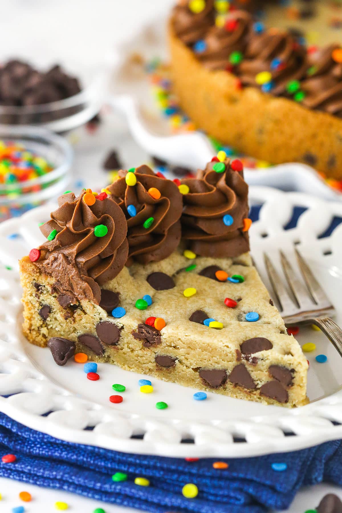 Chocolate chip cookie cake is so moist and chewy and is absolutely loaded with chocolate chips. It's even topped with chocolate buttercream! A slice of Chocolate Chip Cookie Cake with a fork on a white plate.