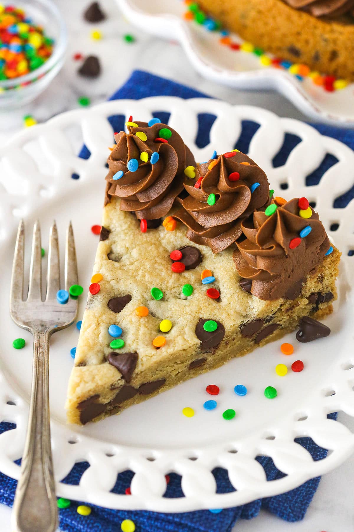 Chocolate chip cookie cake is so moist and chewy and is absolutely loaded with chocolate chips. It's even topped with chocolate buttercream! A slice of Chocolate Chip Cookie Cake with a fork on a white plate.