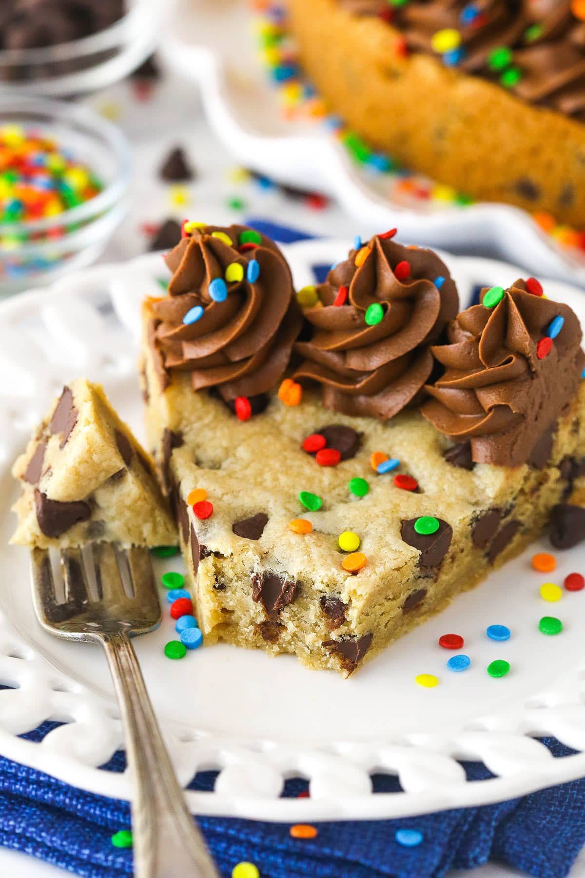A slice of Chocolate Chip Cookie Cake with a bite removed on a white plate.