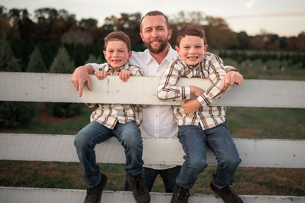 boys sitting on fence smiling with dad