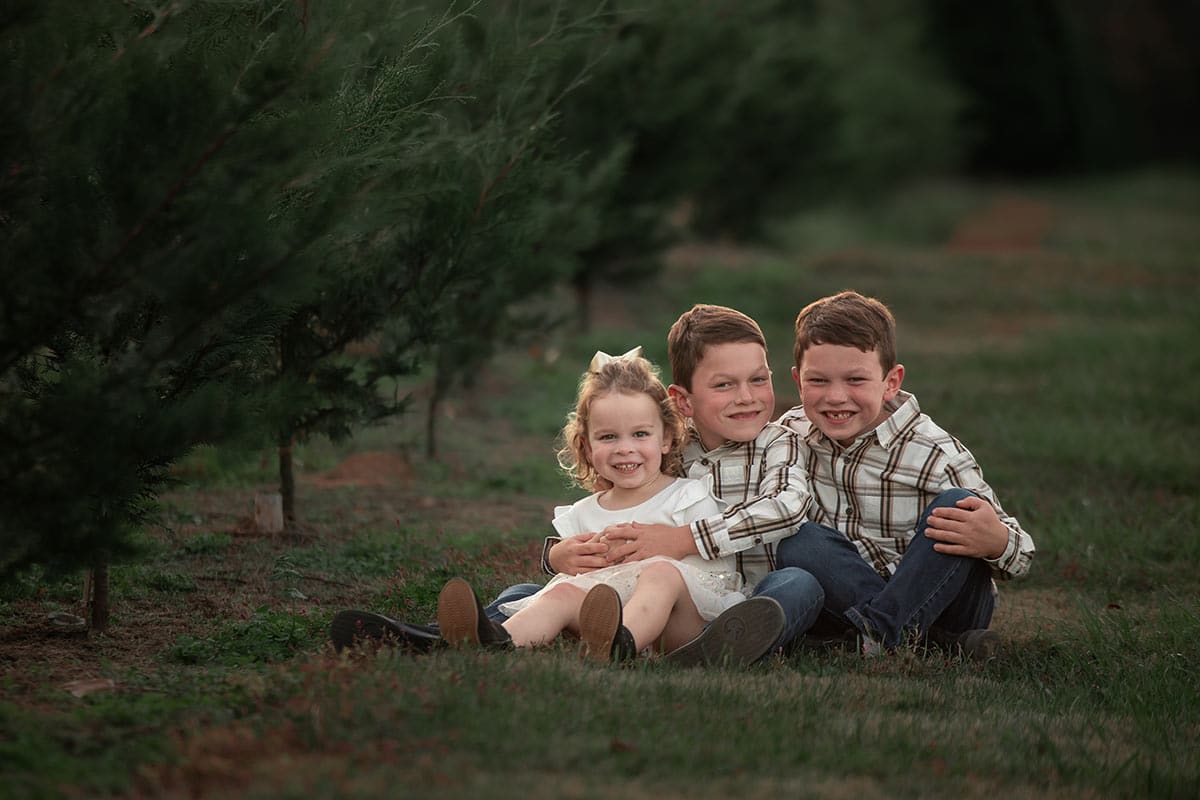 kids sitting on ground between Christmas trees