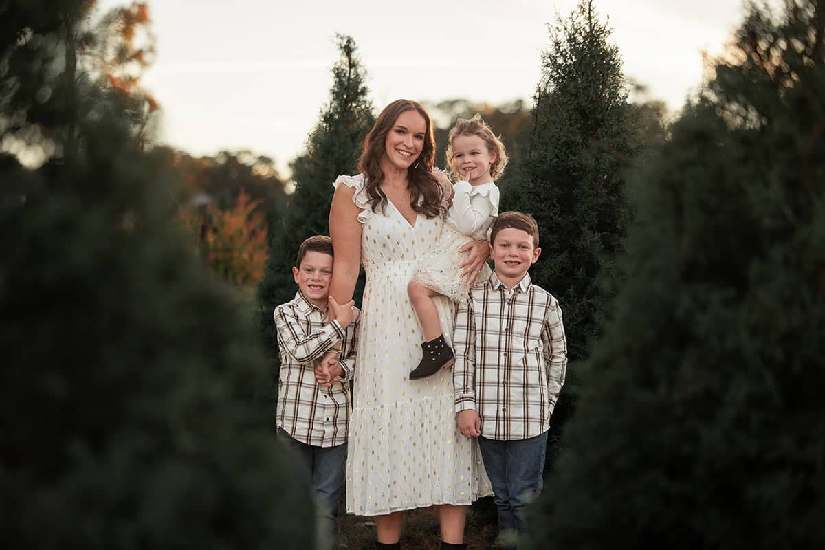 Mom and 3 kids standing in Christmas trees