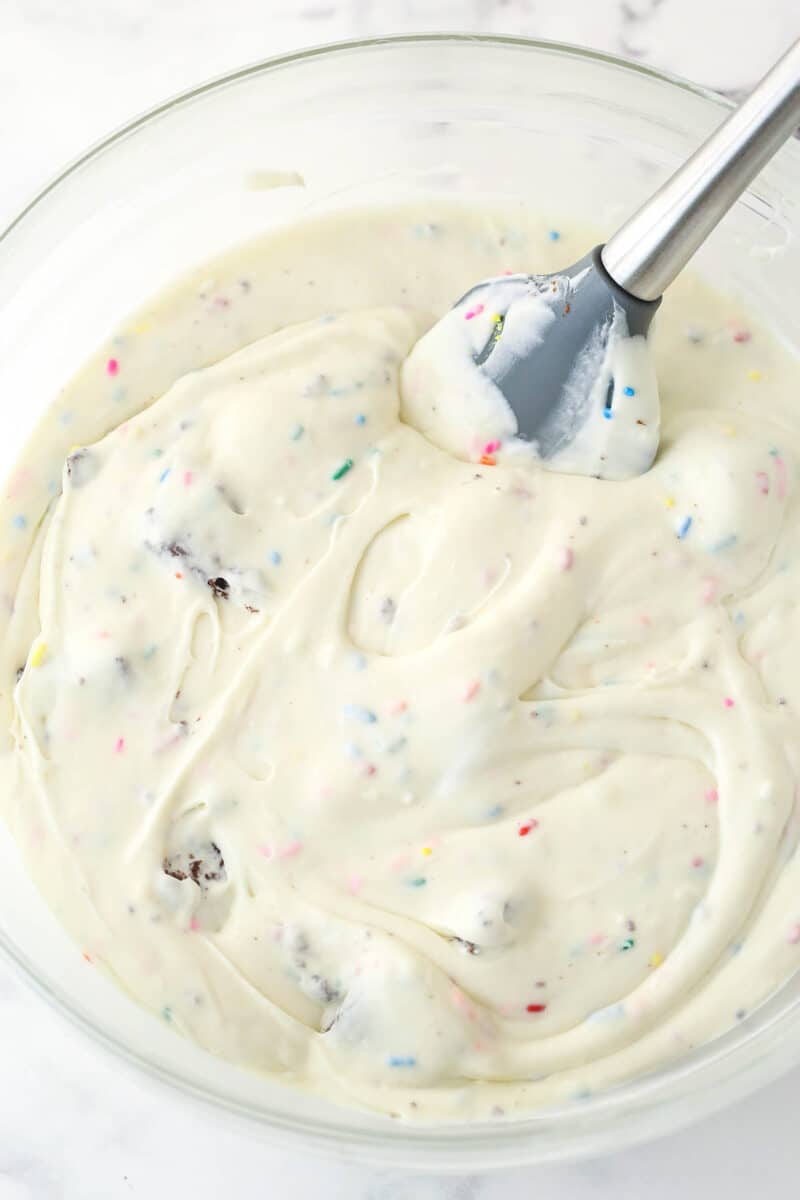Stirring rainbow sprinkles and brownie chunks into birthday cake ice cream.